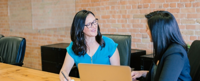 woman in teal t-shirt sitting beside woman in suit jacket